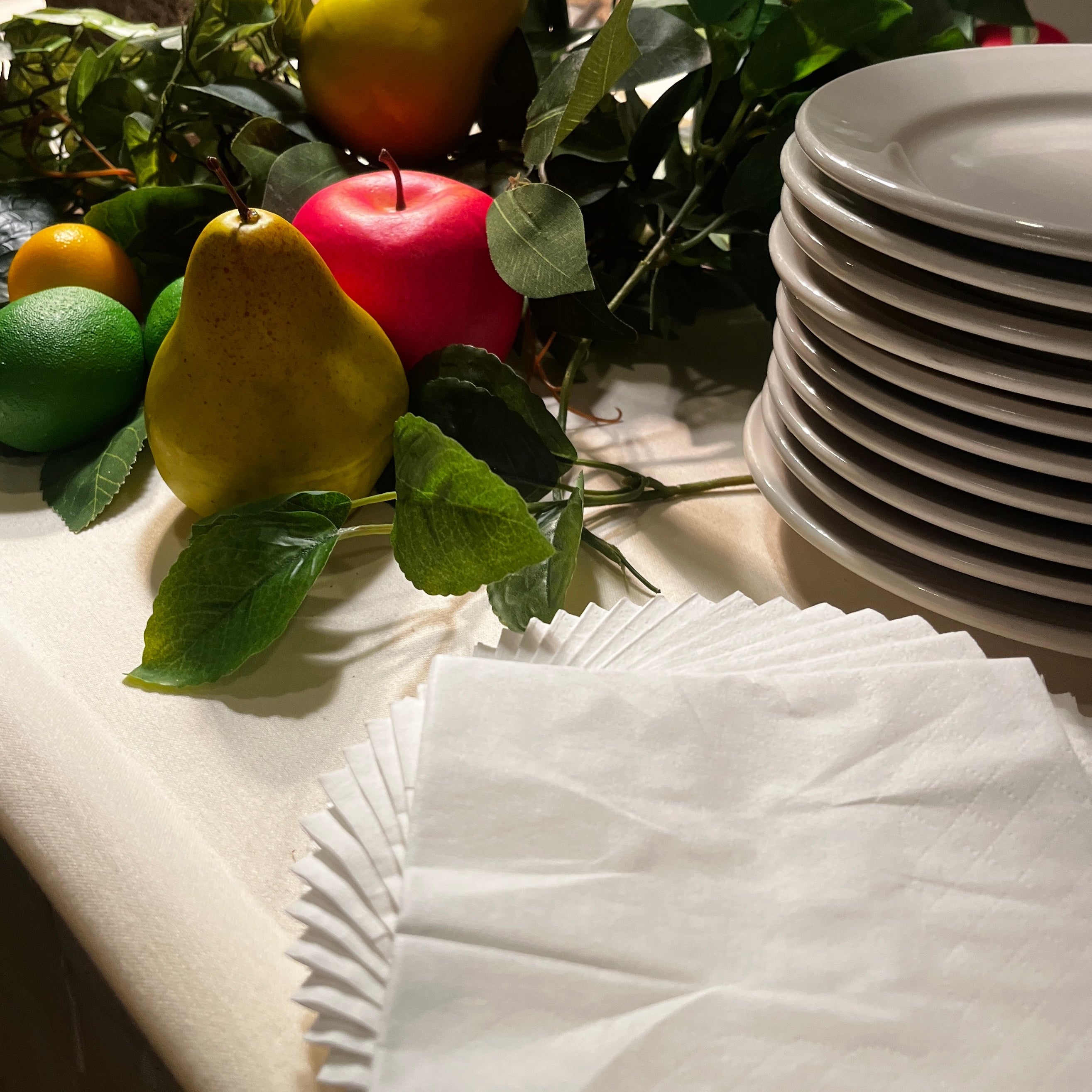 Table setting with fruits, greenery, and stacked plates on a table.